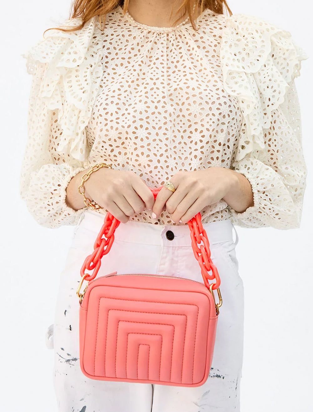 Model holding Clare V.'s shortie strap in bright coral attached to a bag.