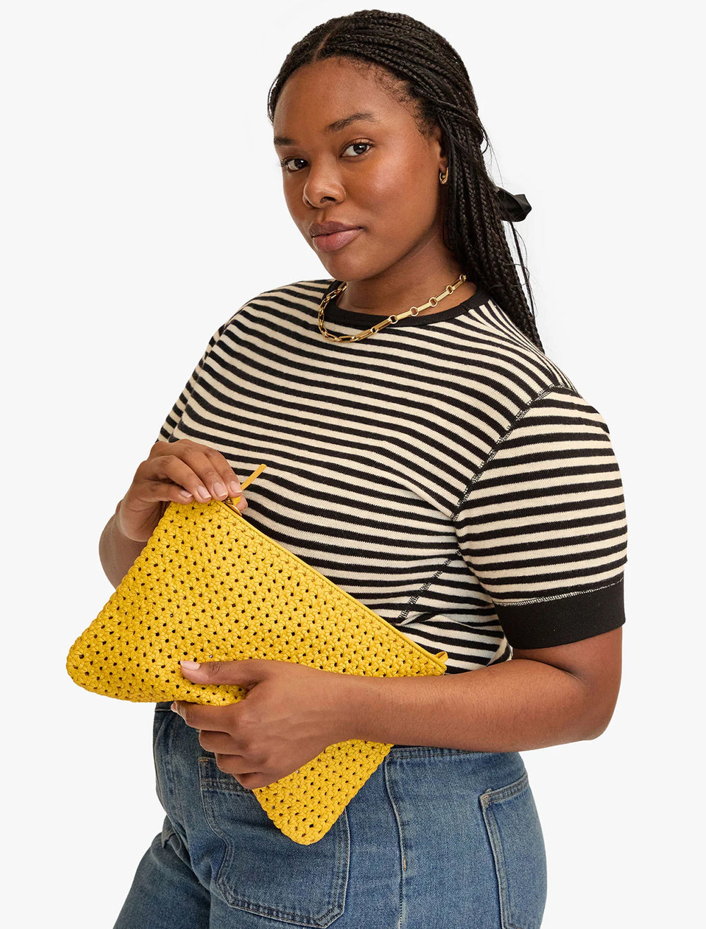 Model carrying Clare V.'s flat clutch with tabs in dandelion rattan.