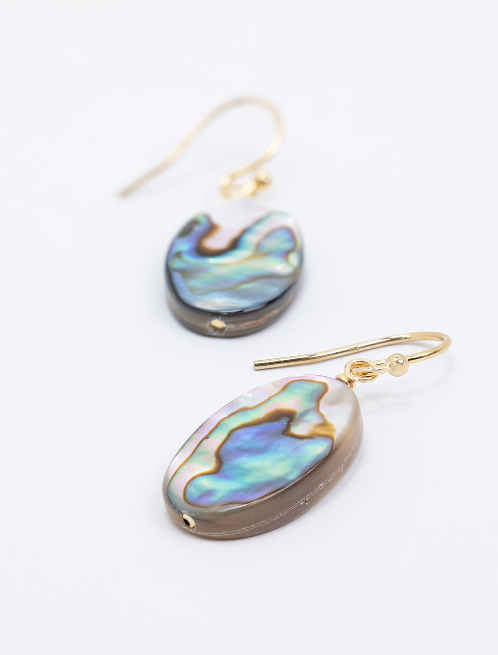 Close-up laydown of AV Max's oval abalone and mother of pearl earrings.