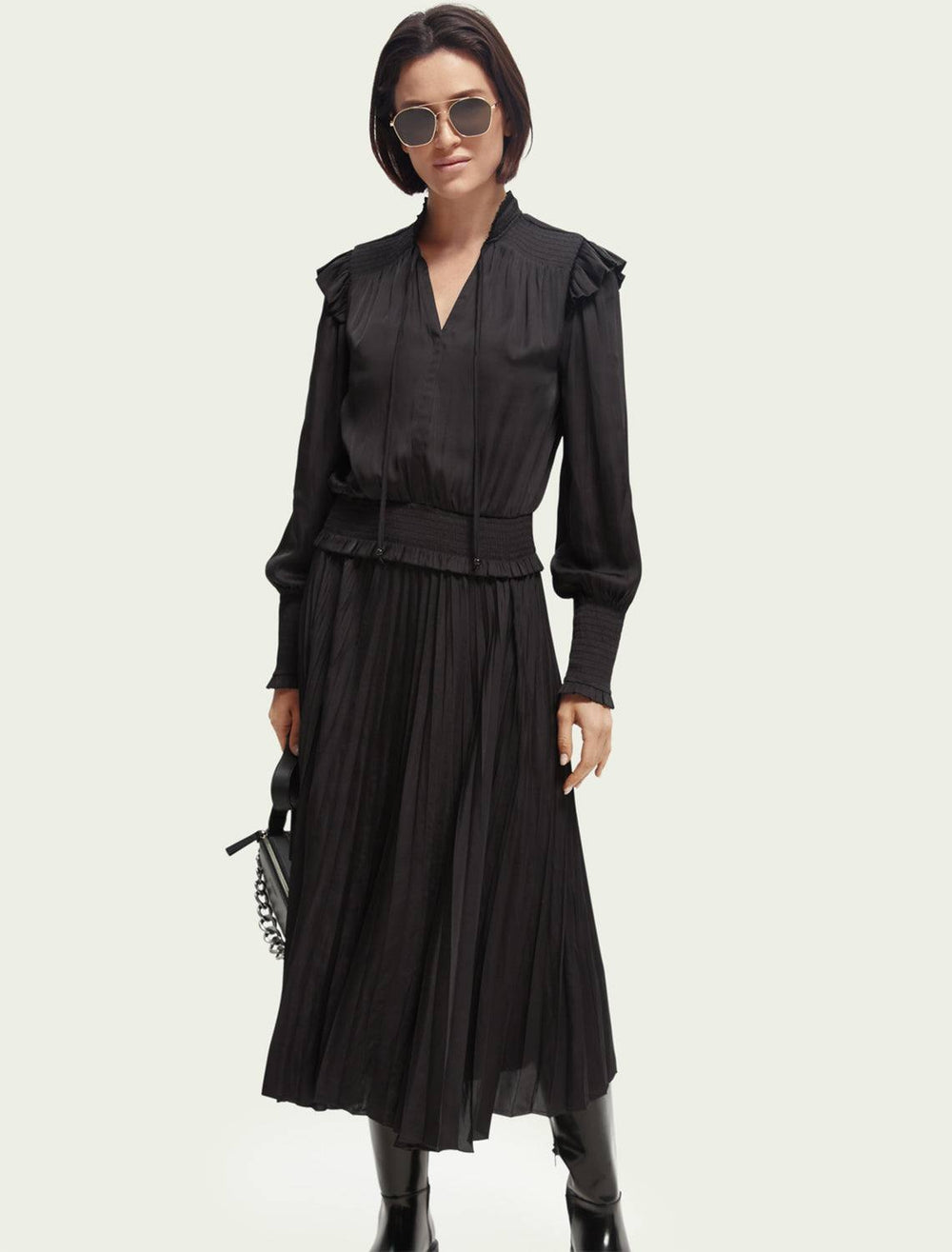 Model wearing Scotch & Soda's Smock Stitch Midi Dress in Black Sky. Model styles the dress with a black handbag, sunglasses, and a pair of black boots.