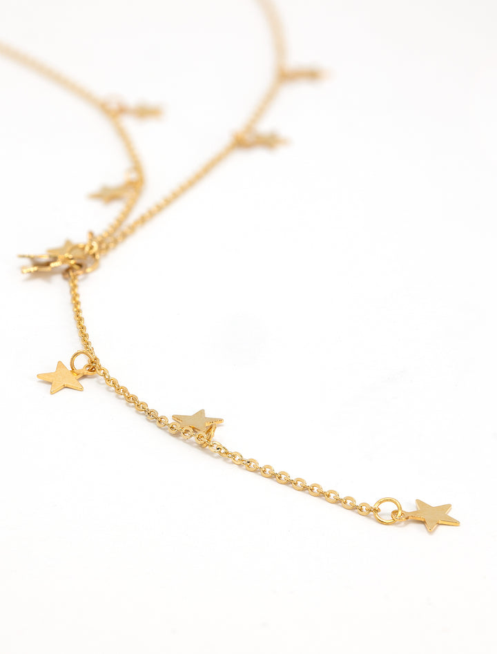 Stylized laydown of AV Max's mini star Y necklace in gold.