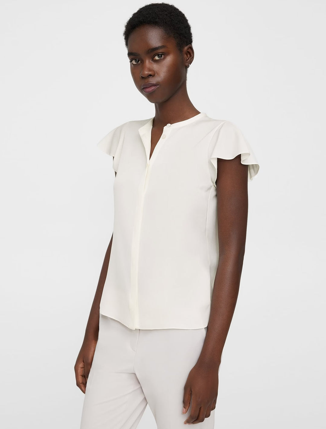 Model wearing Theory's ruffle sleeve top in ivory.