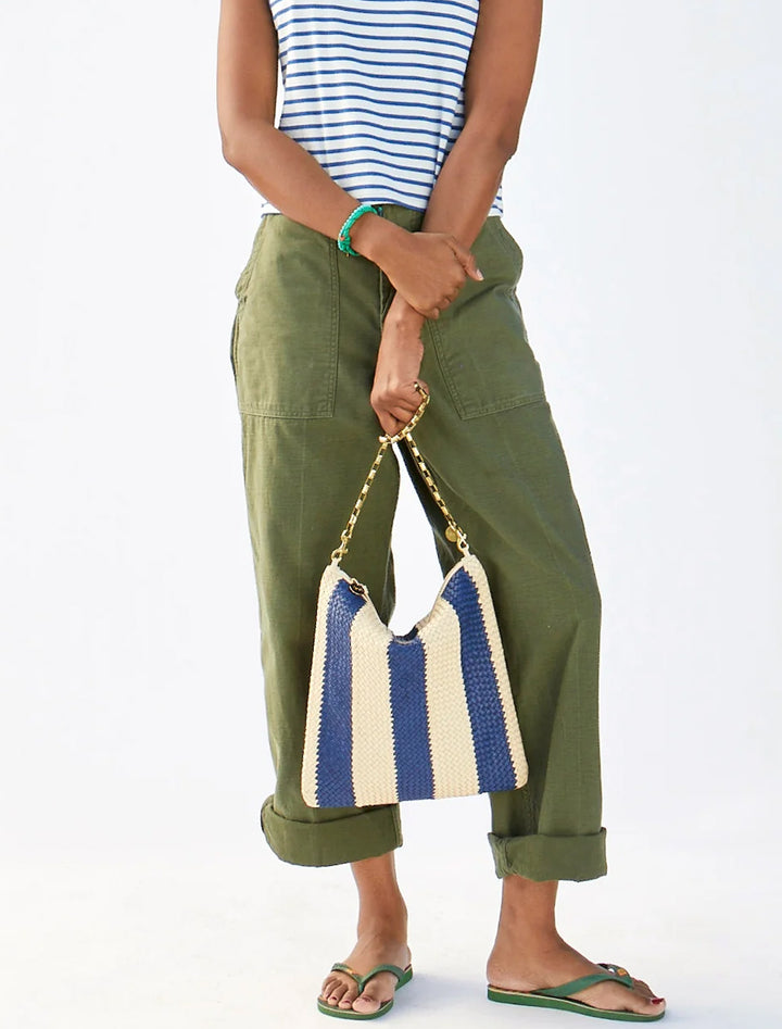 Model holding Clare V.'s foldover clutch with tabs in indigo and cream woven racing stripes.
