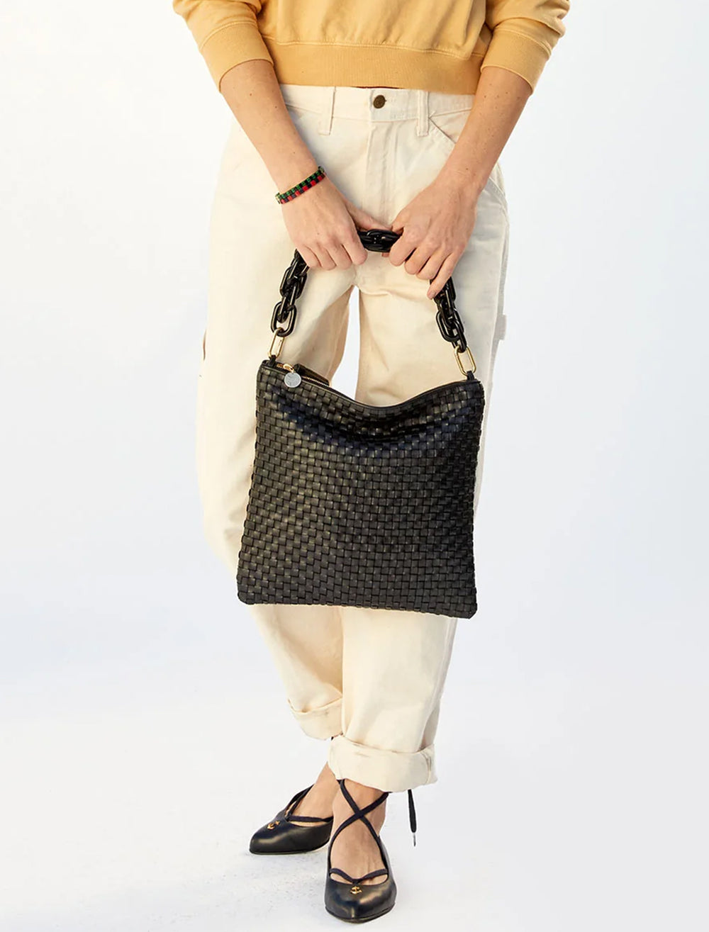 Model holding Clare V.'s foldover clutch with tabs in black woven checker