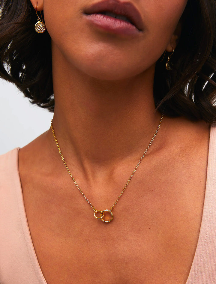 Model wearing Anna Beck's intertwined circles charity necklace in gold.
