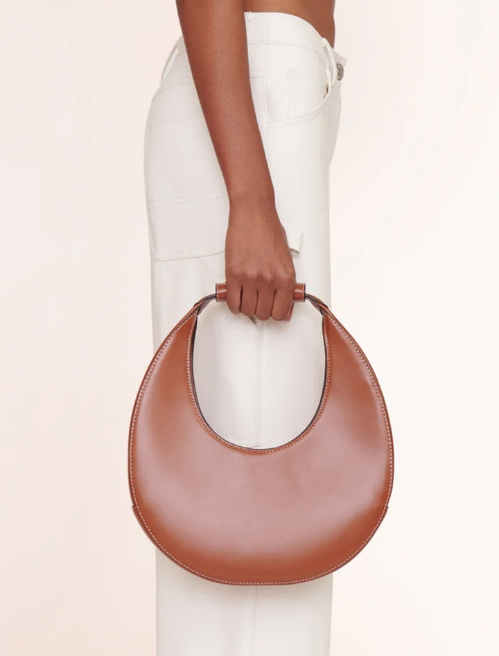 Model holding Staud's moon tote bag in tan.