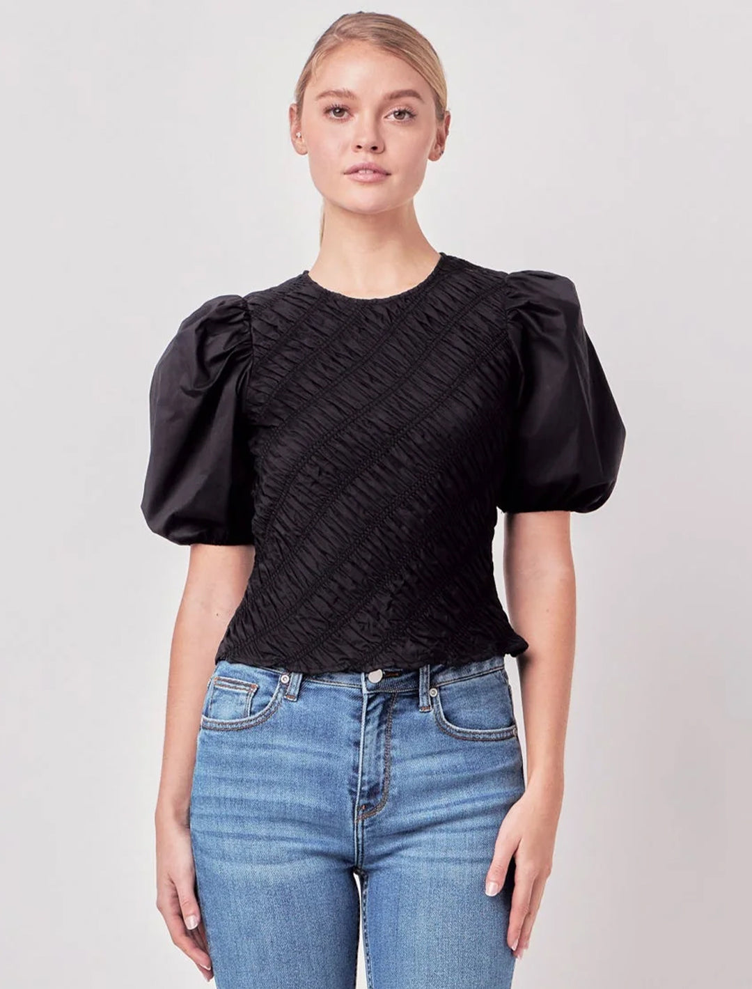 Model wearing English Factory's asymmetrical smocked top in black.
