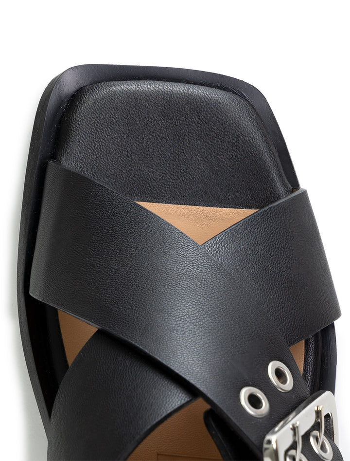 Close-up view of GANNI's black cross strap buckle sandals.