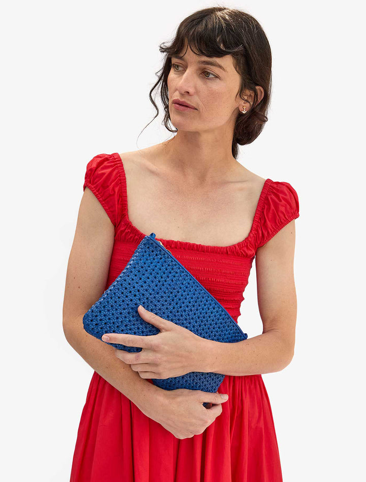 Model holding Clare V.'s flat clutch with tabs in cobalt rattan.