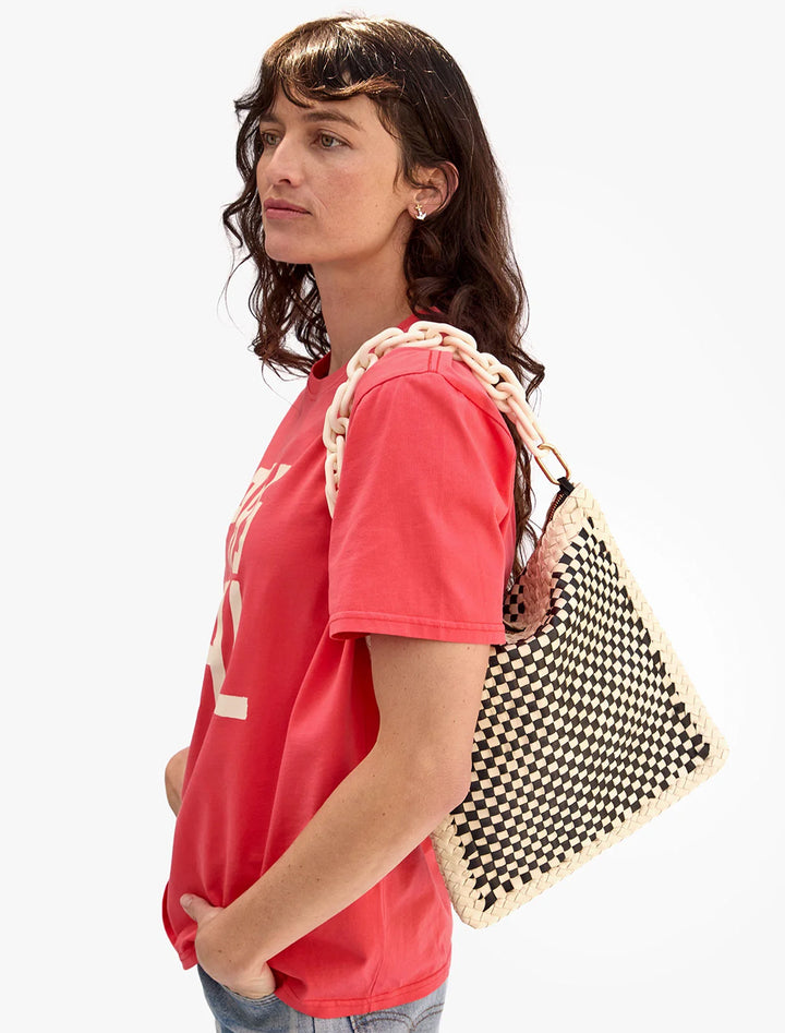 Model wearing foldover clutch with tabs in black and cream border woven with a shoulder strap.