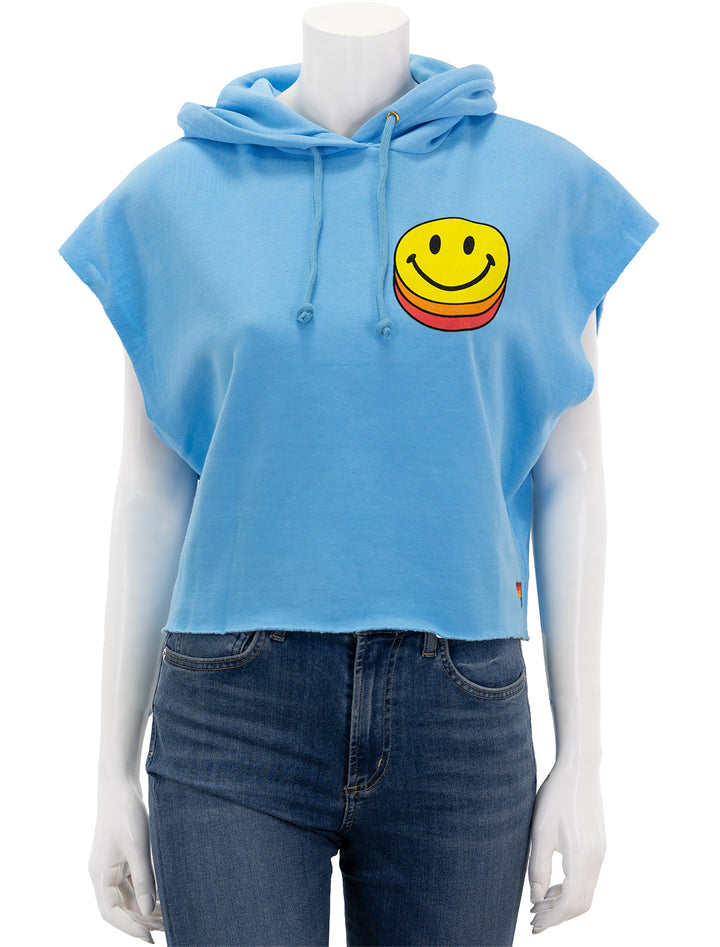 Front view of Aviator Nation's smiley sunset sleeveless cropped pullover hoodie in sky.