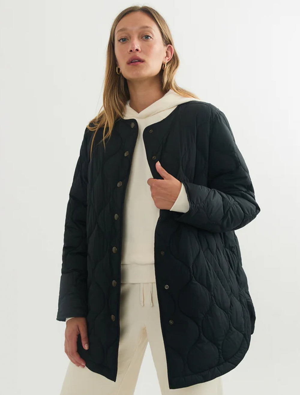 Model wearing Marine Layer's mid length quilted coat in black.