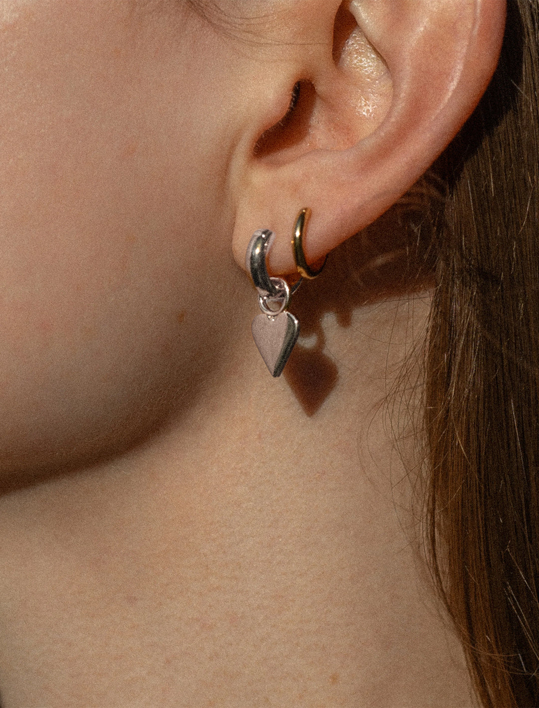 Model wearing THATCH's petite heart earrings in silver.