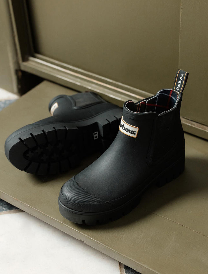 Stylized laydown of Barbour's halton chelsea welly boot in black.