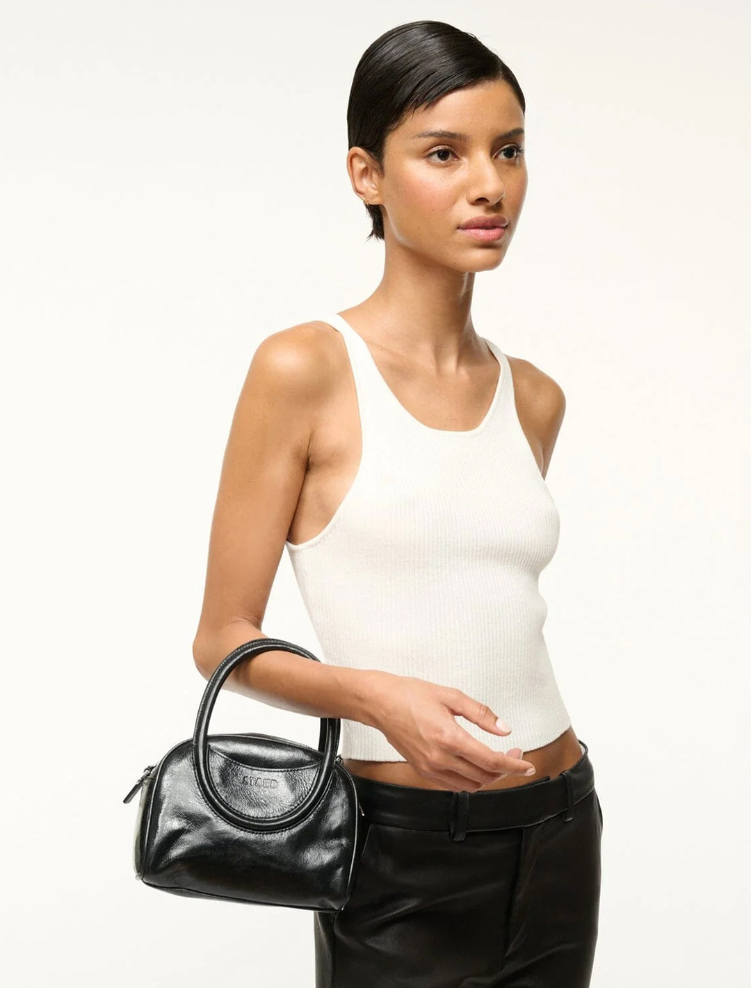 Model carrying Staud's maude mini bowler bag in black.