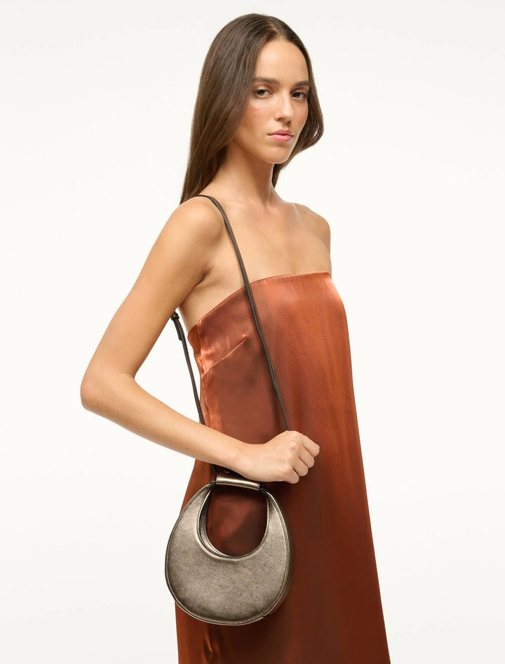 Model wearing Staud's good night moon bag in aged bronze on her shoulder.