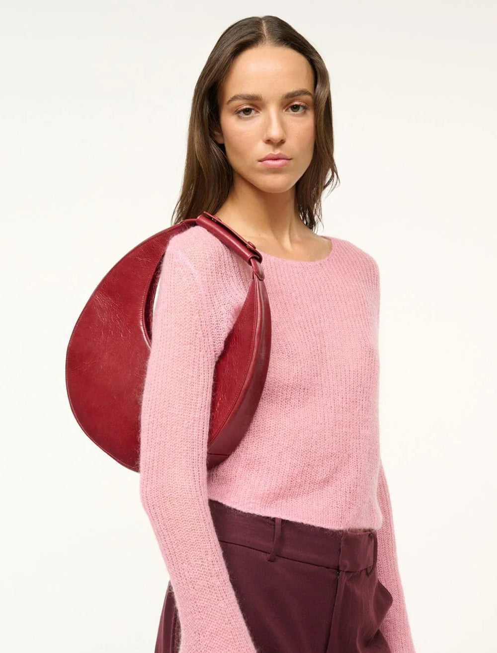 Model wearing Staud's moon tote bag in pinot on her shoulder.