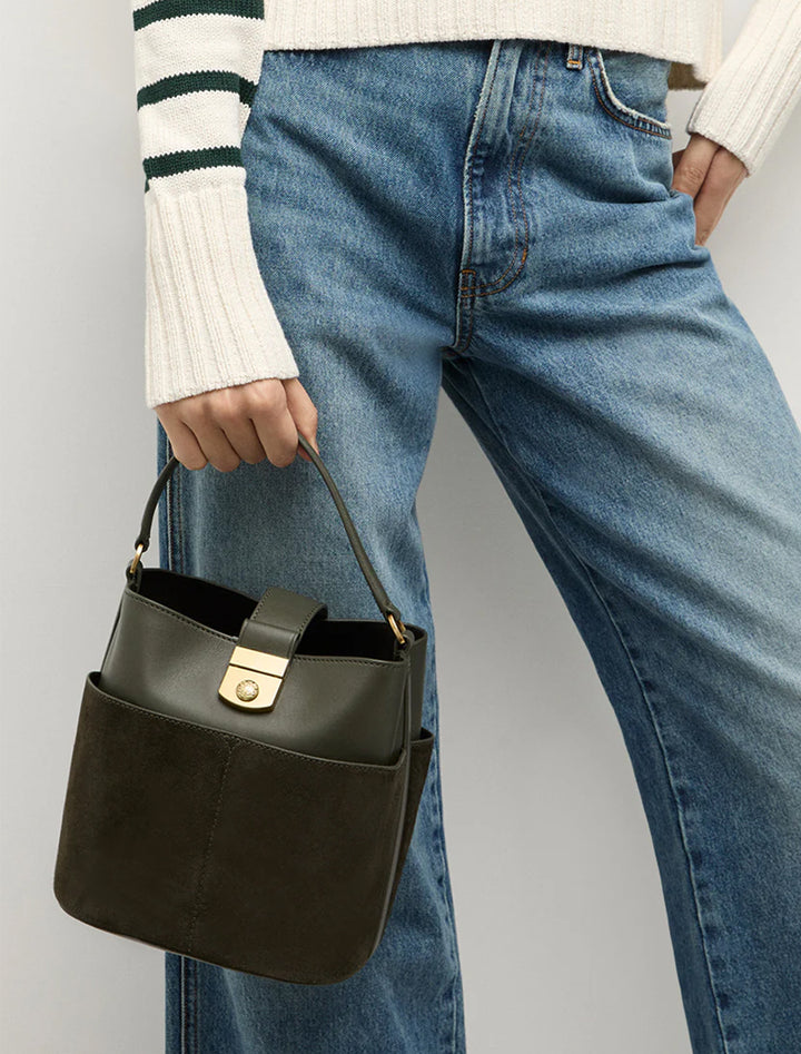 Model holding Veronica Beard's the small crest lock bucket bag in pine.