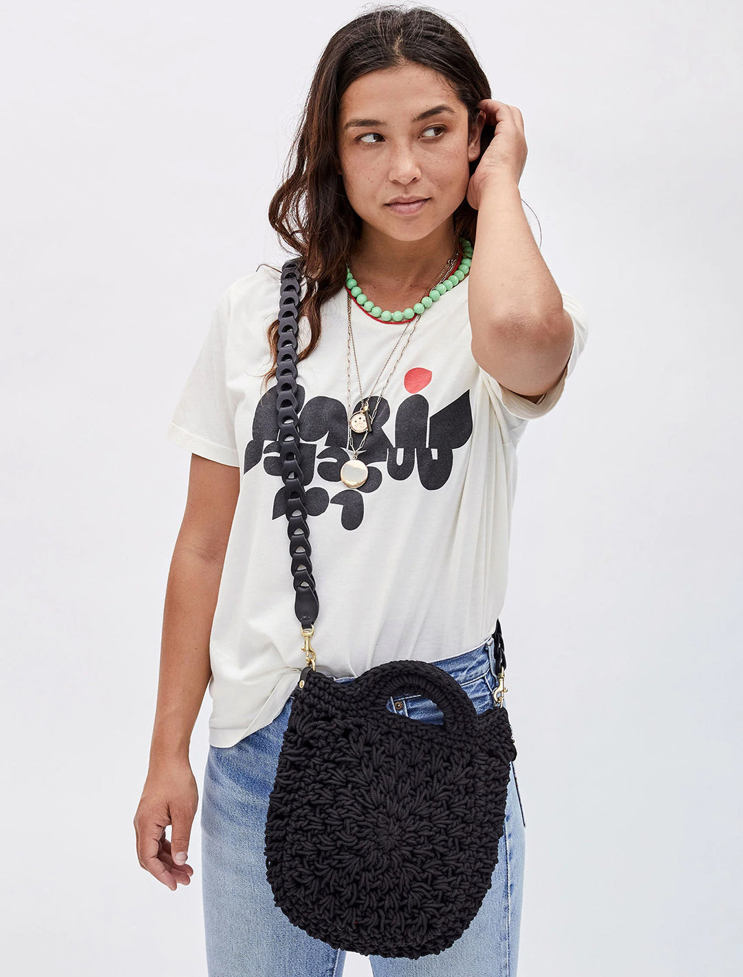 Model wearing Clare V.'s crossbody link strap in black attached to a black bag.