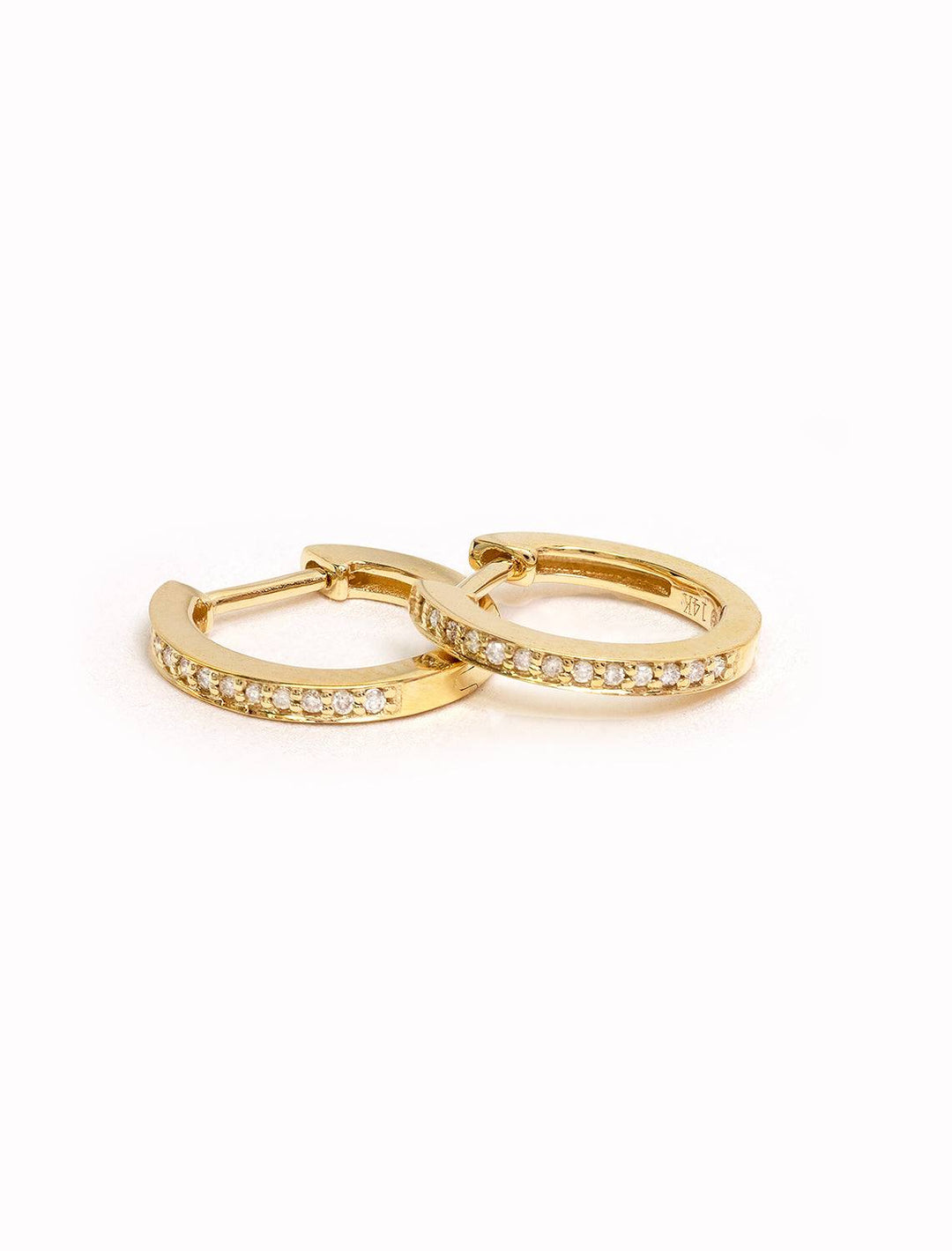 Stylized laydown of Sydney Evan's pave huggie hoops in yellow gold.
