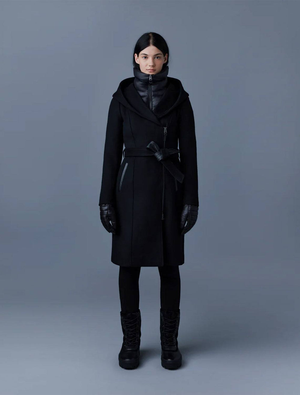 model wearing shia coat in black with leather trim with black gloves, pants, and boots