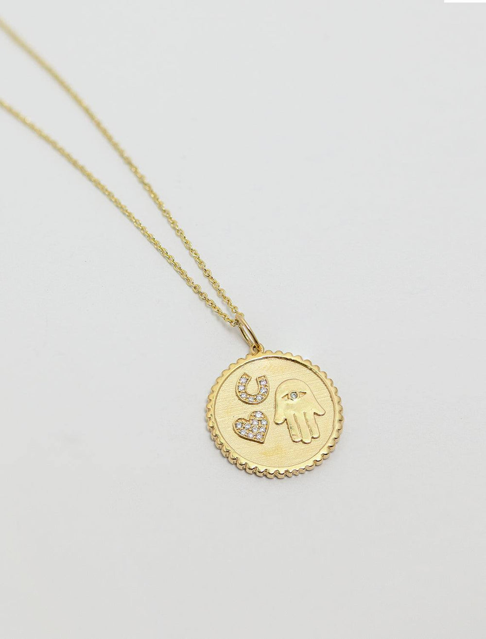 a detailed top down view of the luck and protection coin charm. the coin has a lattice edge and raised edges of the heart, horseshoe and hamsa hand