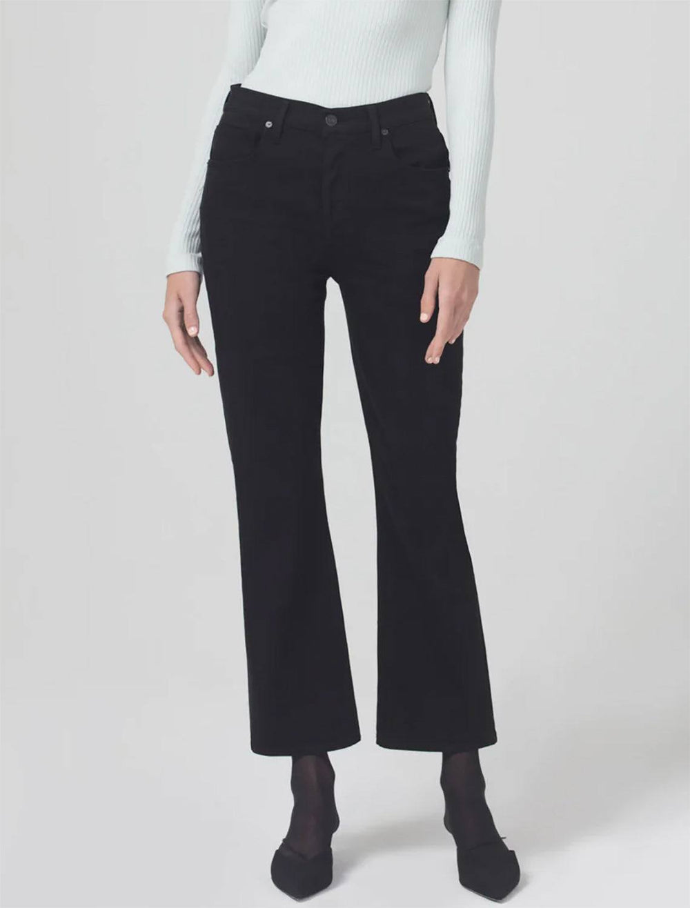 Model wearing Citizen of Humanity's Isola Cropped Boot in Plush Black. Model pairs the pants with a light blue ribbed long sleeve shirt and black heels.