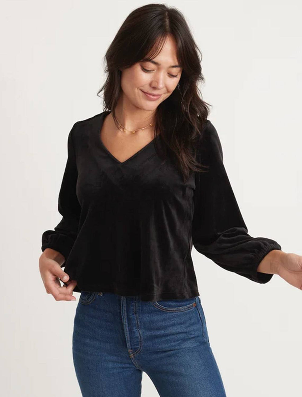 Model wearing Marine Layer's velour v neck top in black. Model pairs the shirt with blue jeans.
