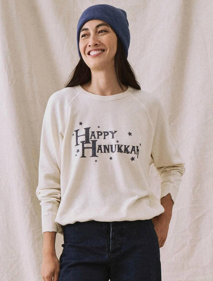 Model wearing The Great's happy hanukkah college sweatshirt in washed white.