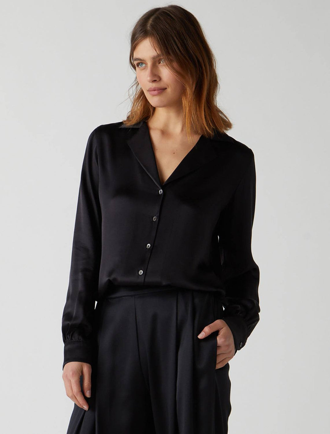 Model wearing Velvet's Soho Blouse in Black. Model pairs the blouse with matching slacks.