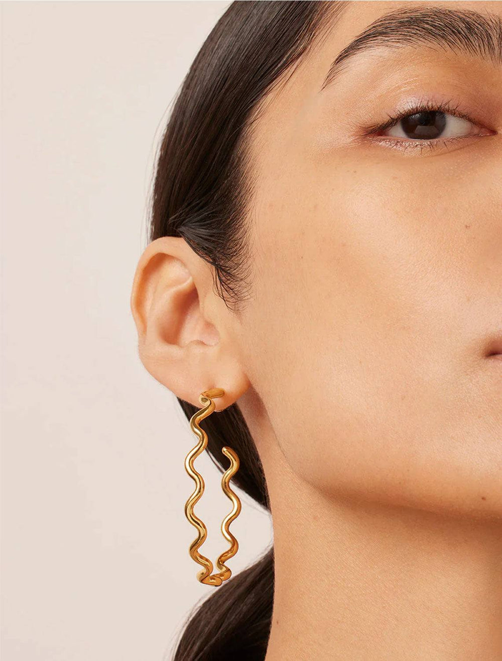 Model wearing Jenny Bird's squiggle hoops in gold.