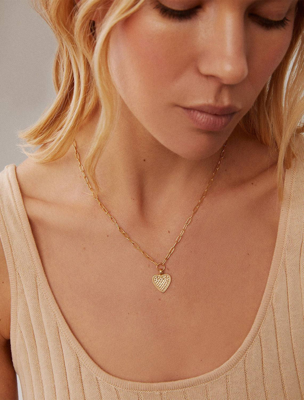 Model wearing Anna Beck's medium heart engravable necklace in gold.