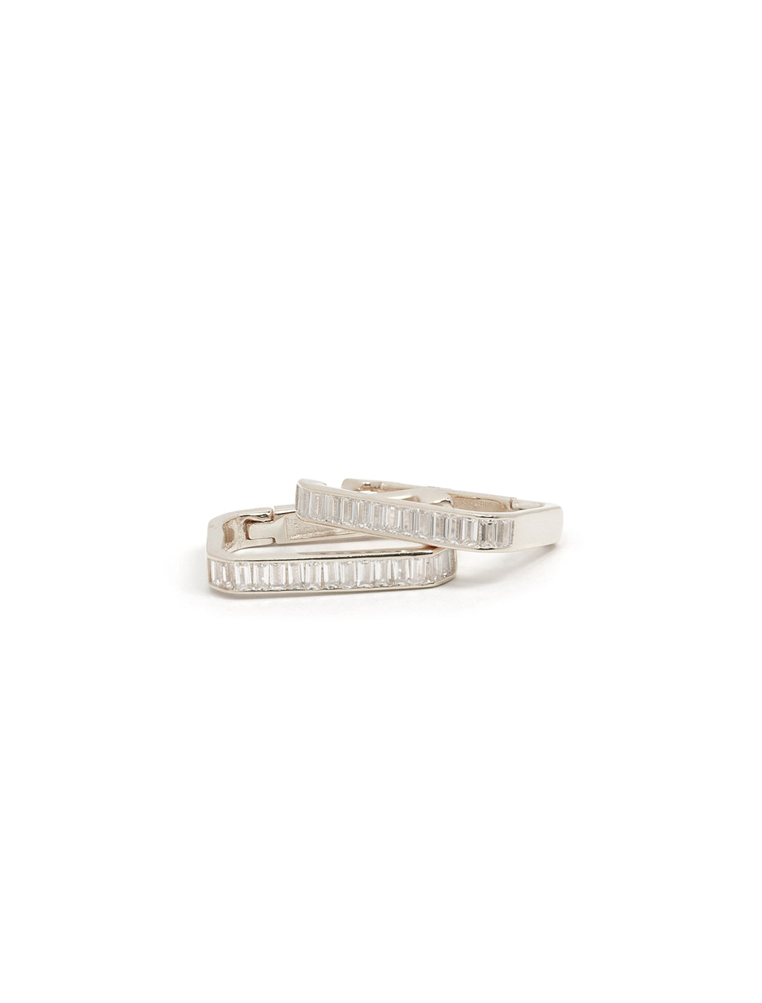 Stylized laydown of Tai's oval baguette huggies in silver.